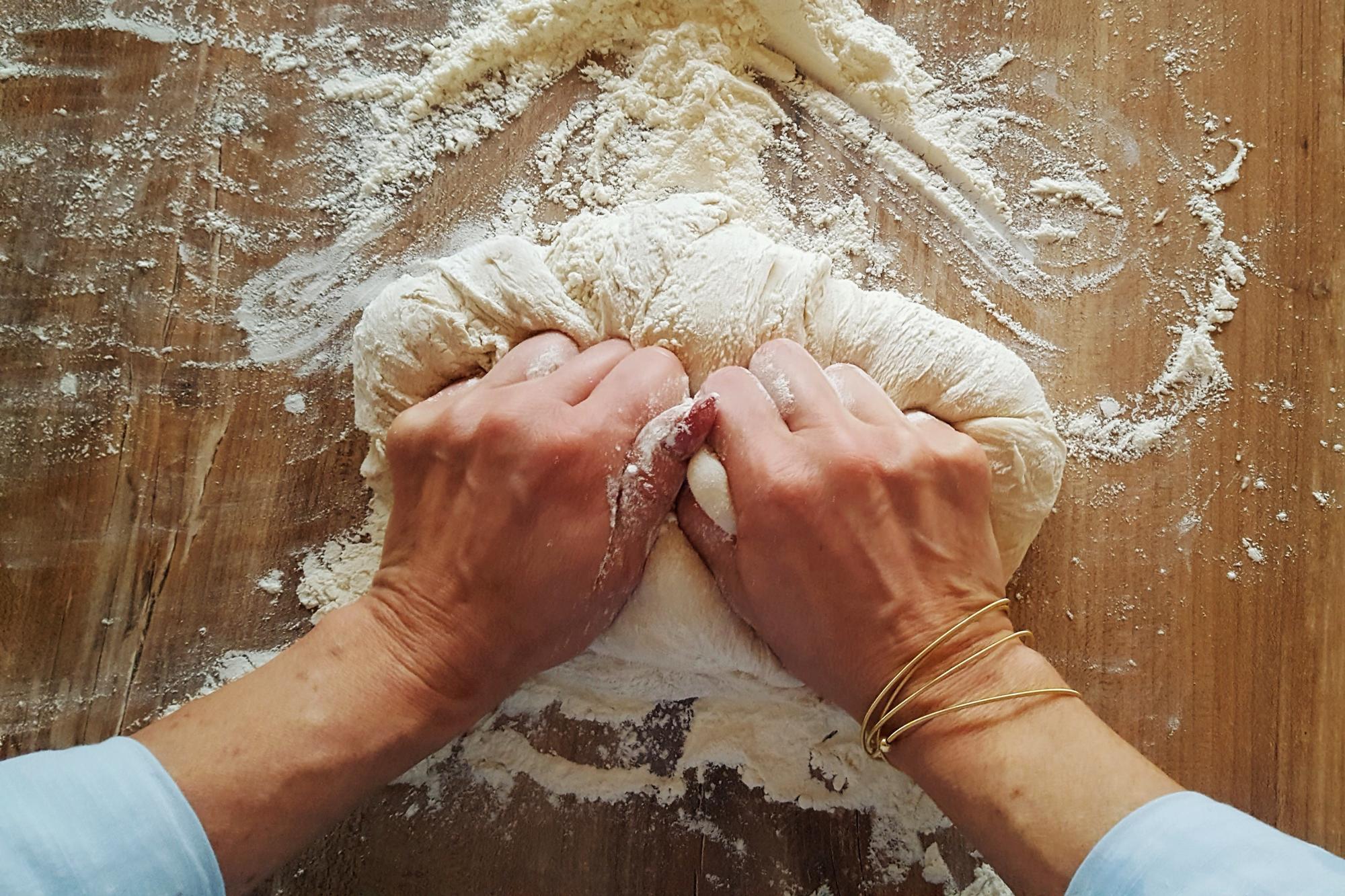 Close up of hands kneading dough on wooden board